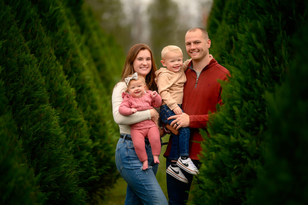 family with small children standing in christmas tree farm.
